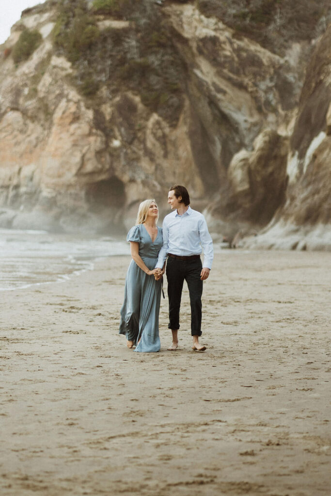 Couple holding hands while walking across Hug Point during their engagement photo session