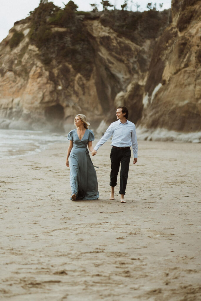 Couple holding hands while walking across Hug Point during their engagement photo session
