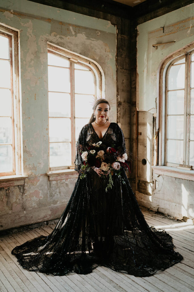 Bride wearing black lace wedding dress and holding a dark wedding floral bouquet