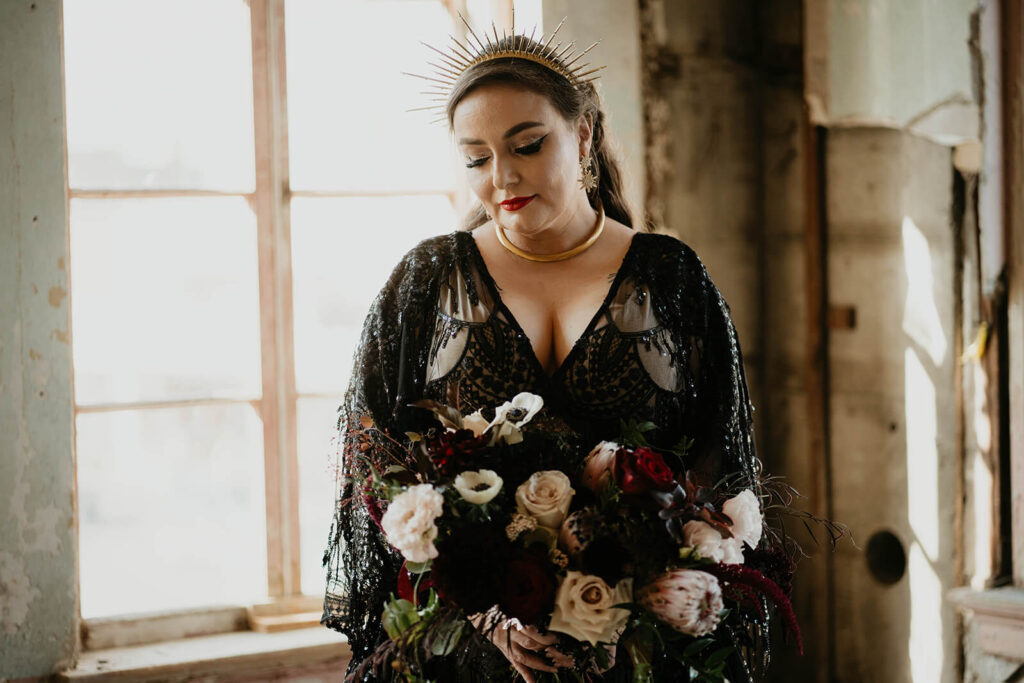 Bride wearing black lace wedding dress and holding a dark wedding floral bouquet