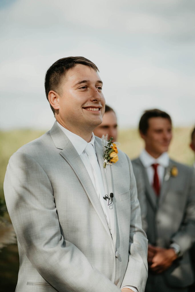 Groom smiling at bride walks down outdoor wedding aisle