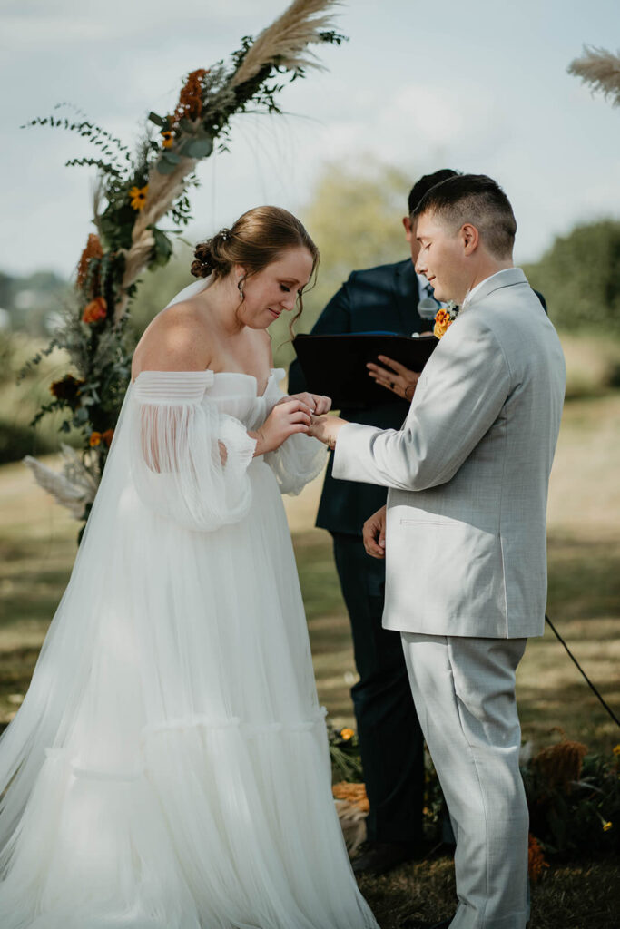 Bride putting ring on groom's finger at outdoor wedding ceremony