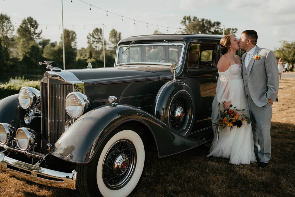 Bride and groom kissing next to vintage car at Pemberton Farm wedding