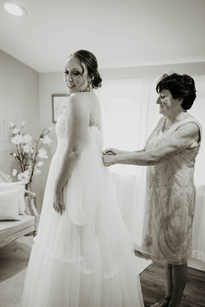 Bride's mother helping her into romantic flowy wedding dress