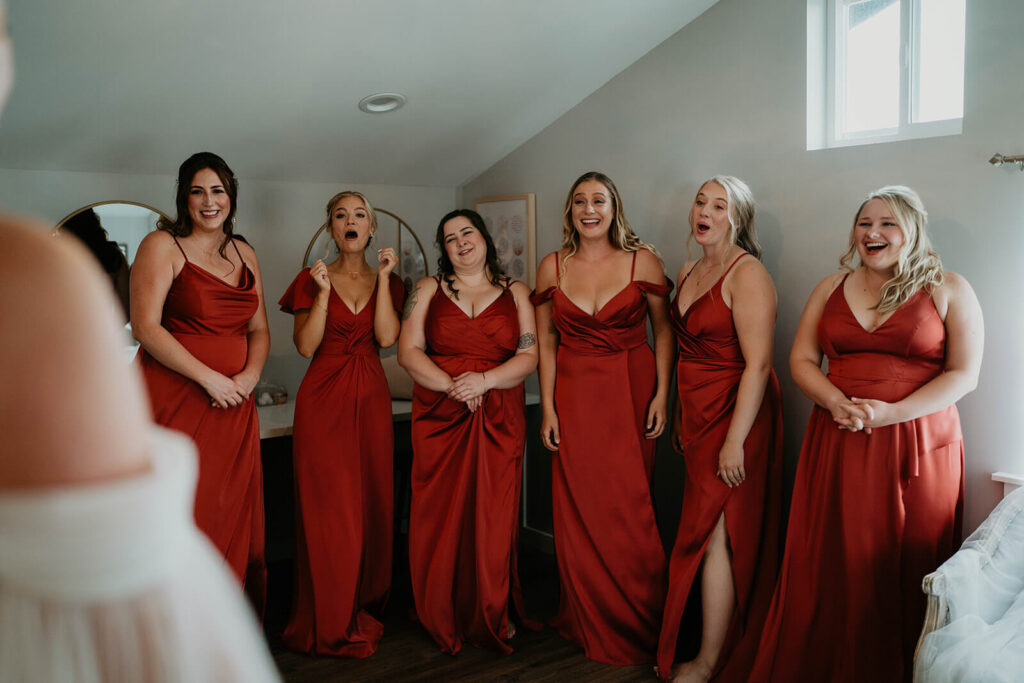 Bridesmaids wearing burnt orange dresses react during first look with bride