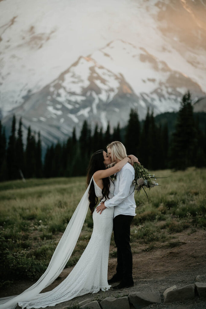 Two brides kissing on a trail in front of Mt Rainier