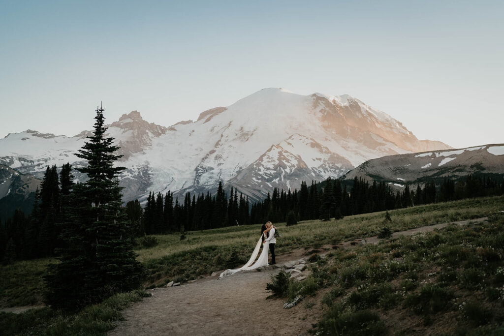 Two brides kissing on a trail in front of Mt Rainier