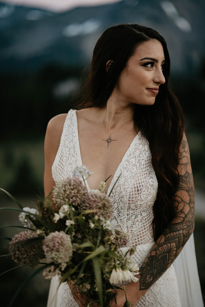 Bride wearing white lace v-neck wedding dress while holding a wildflower bouquet at Mt Rainier