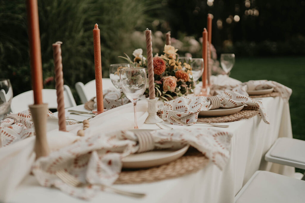White reception table and chairs with orange and brown candlesticks and white place settings with patterned napkins