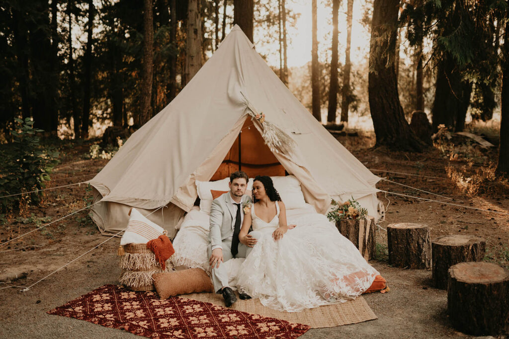 Bride and groom sit in front of a boho tent in the woods for their CedarVale Events woodland themed wedding