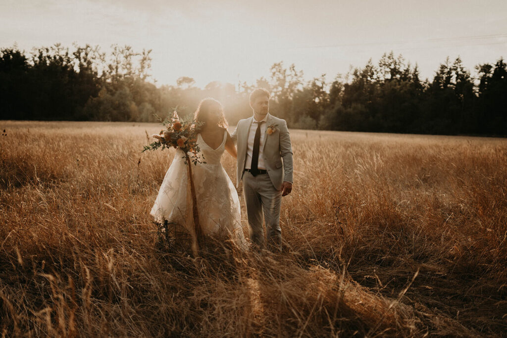 Bride and groom walk through the meadow at sunset during their woodland themed wedding at CedarVale Events