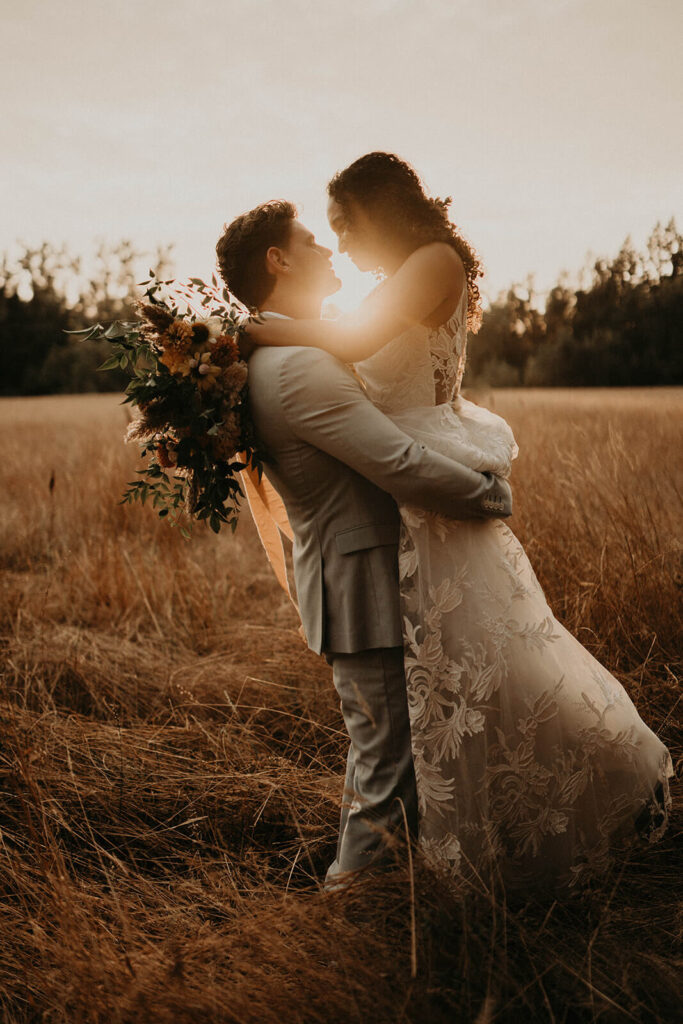 Groom picks up bride during sunset portraits in the meadow at CedarVale Events wedding in Oregon