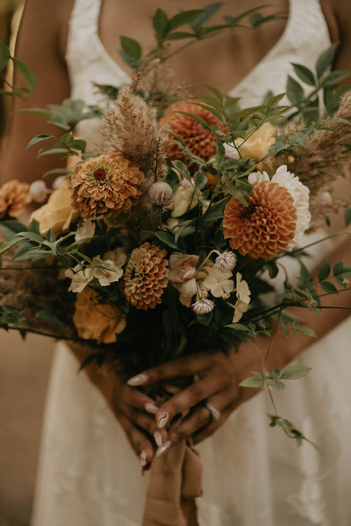 Bride holding a bouquet of orange flowers with greenery while getting ready for first look at woodland themed wedding