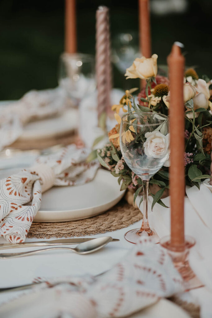 White reception table and chairs with orange and brown candlesticks and white place settings with patterned napkins
