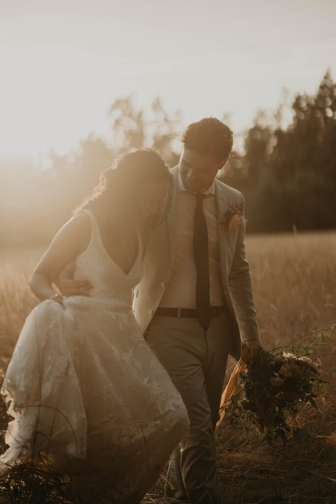 Bride and groom walk through the meadow at sunset during their woodland themed wedding at CedarVale Events