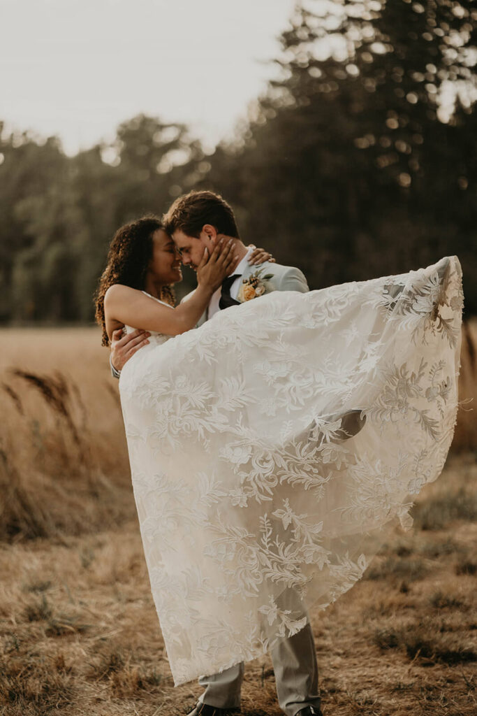 Groom carries bride through the meadow during sunset portraits at woodland themed wedding in Oregon