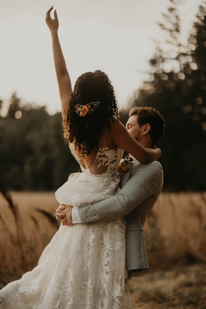 Groom carries bride through the meadow during sunset portraits at woodland themed wedding in Oregon