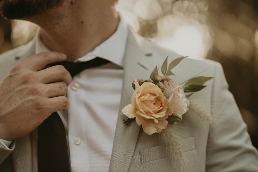 Groom adjusting black tie with beige linen suit at woodland themed wedding in Oregon