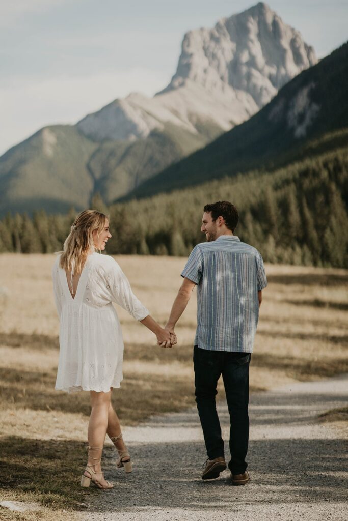 Man and woman holding hands and walking down a trail in the mountains for their adventure engagement photos