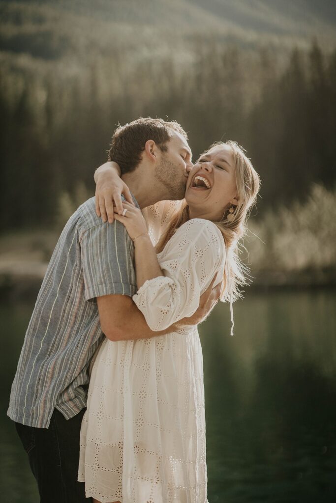 Man kissing woman while she laughs during their adventure engagement photoshoot in the mountains