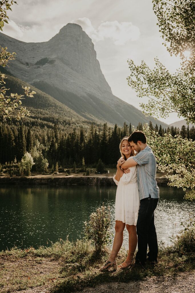 Man and woman hugging by the lake during engagement photos in the mountains