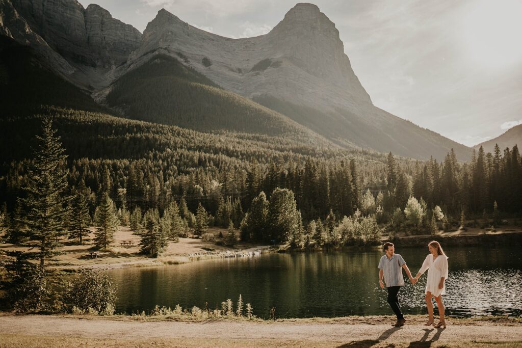 Man and woman walking hand in hand by the lake during summer engagement photos in Banff
