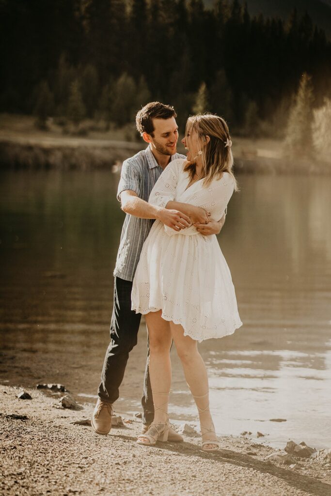 Man and woman hugging and laughing by the lake during engagement photos in the mountains