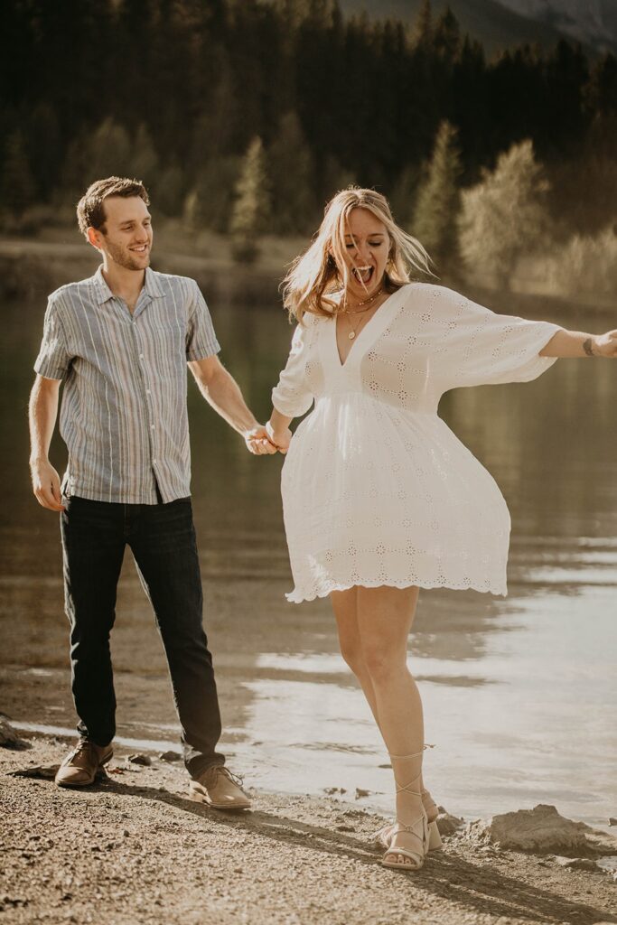 Man and woman dancing by the lake during engagement photos in the mountains
