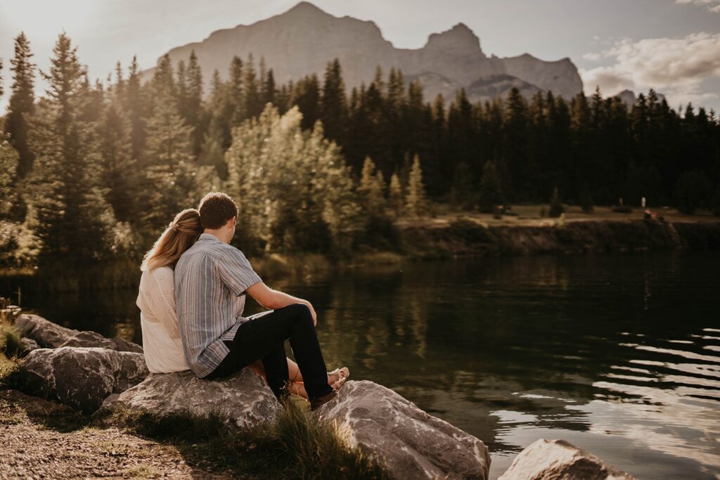 Couple sitting on a rock by the lake during summer engagement photo session