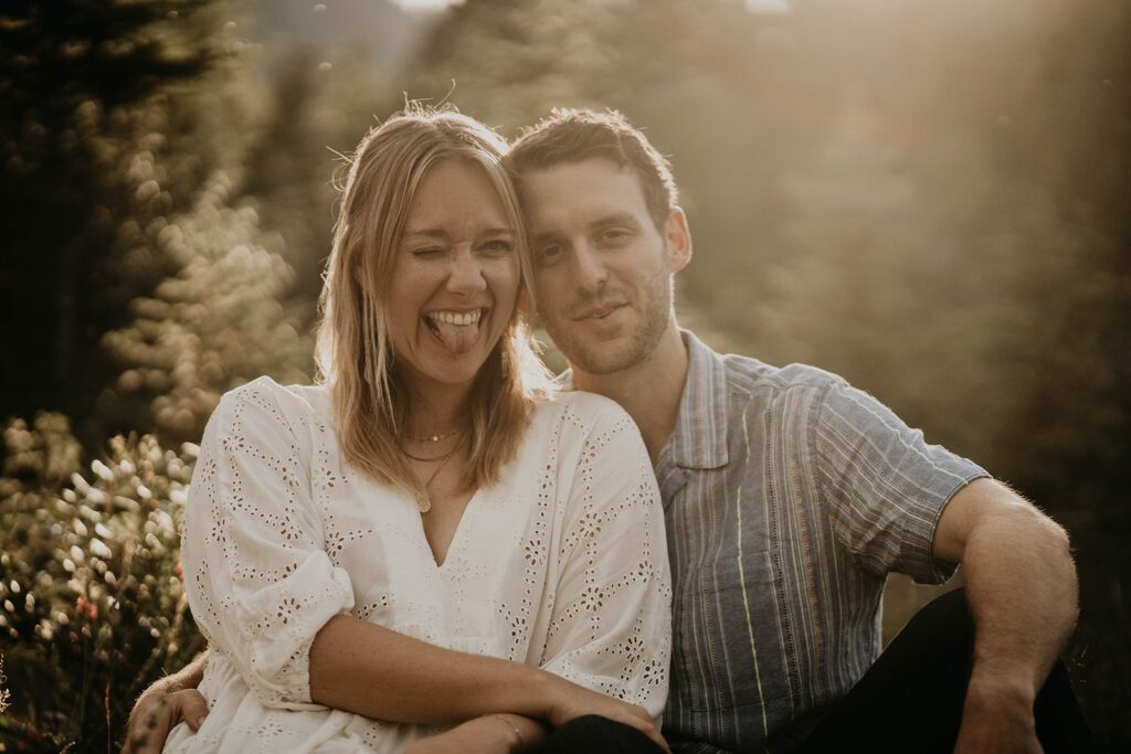 Woman winking at the camera while sitting on the ground with her fiancee for outdoor engagement photos in Banff