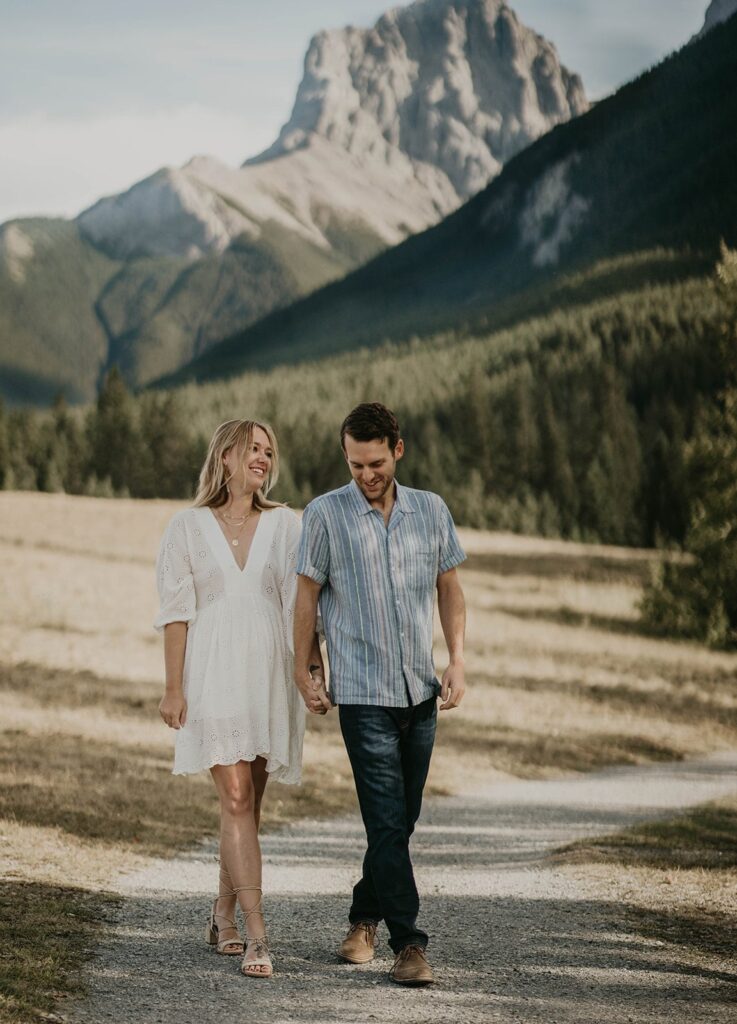 Man and woman holding hands and walking down a trail during destination engagement photos session in Canada