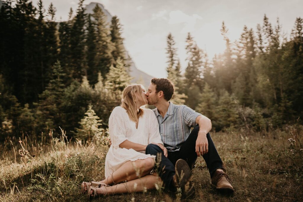 Couple sitting on the ground kissing during their adventure engagement photos in Banff, Canada