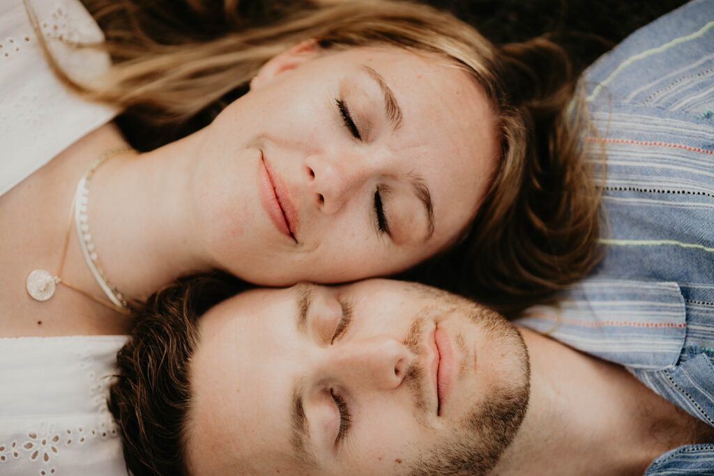 Man and woman laying down on the ground with their eyes closed during their mountain engagement photos in Banff