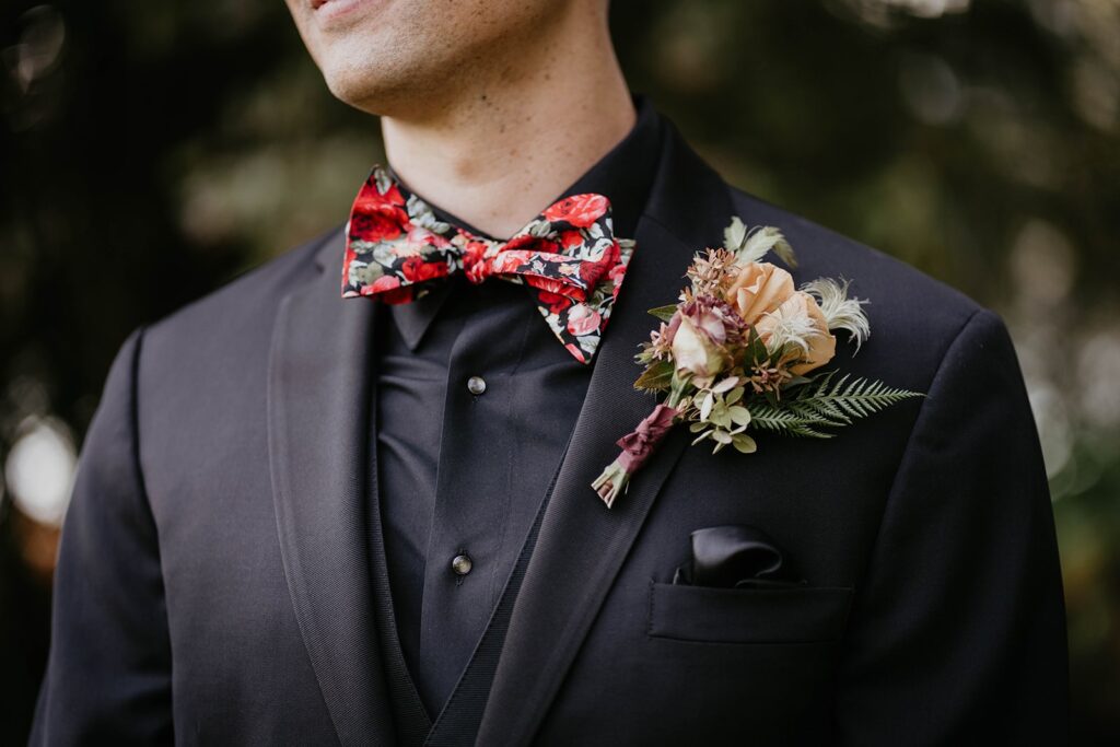 Groom in all black suit with red floral bowtie