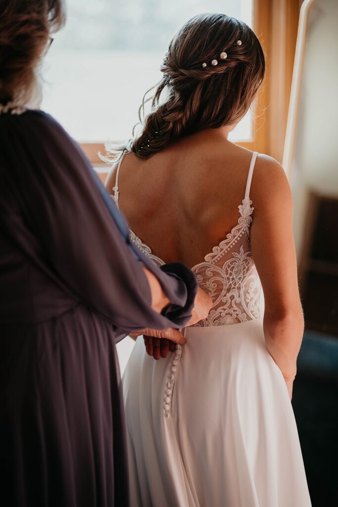 Mother of the bride helping her into her white v-neck backless wedding dress