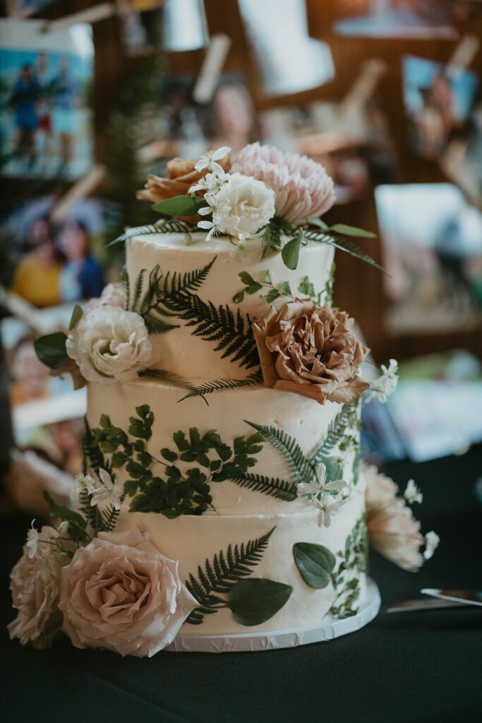 White three-tier wedding cake with fern leaves and white and brown wedding flowers