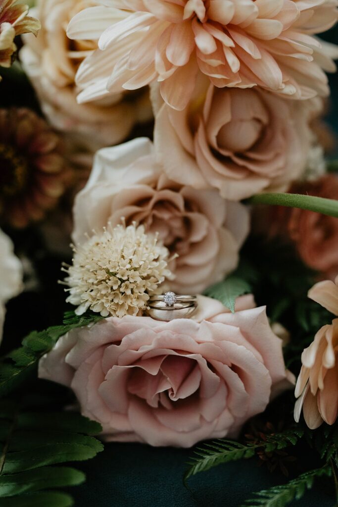 Pink and white wedding flowers with gold and diamond wedding bands resting on top
