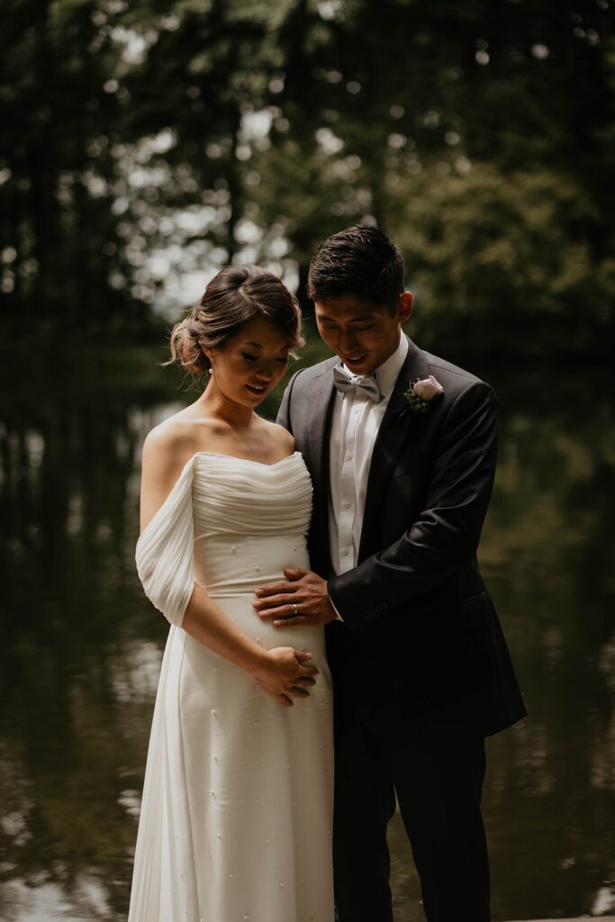 Bride and groom hold bride's pregnant belly at Asian wedding