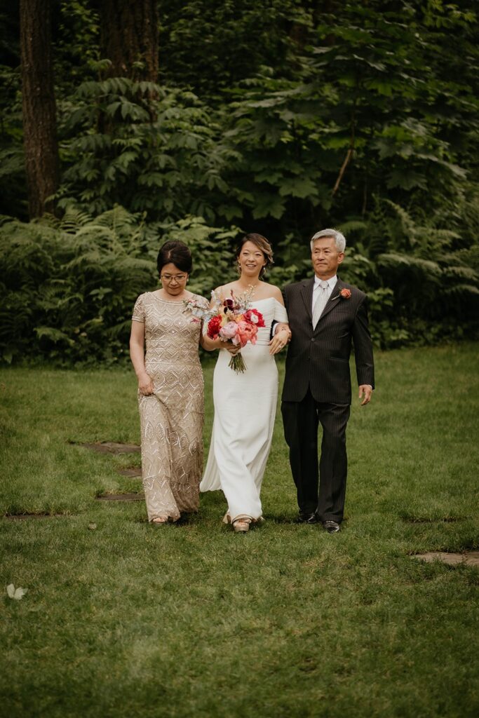 Bride enters the outdoor wedding ceremony with her parents