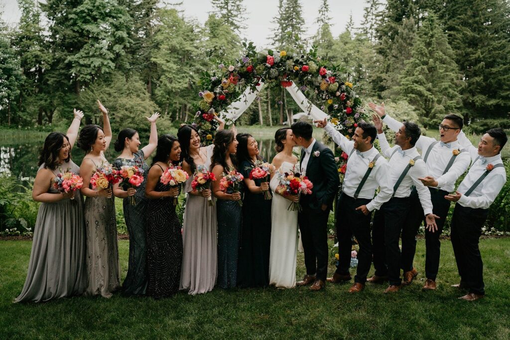Bride and groom kiss while their wedding party cheers at outdoor wedding in Oregon