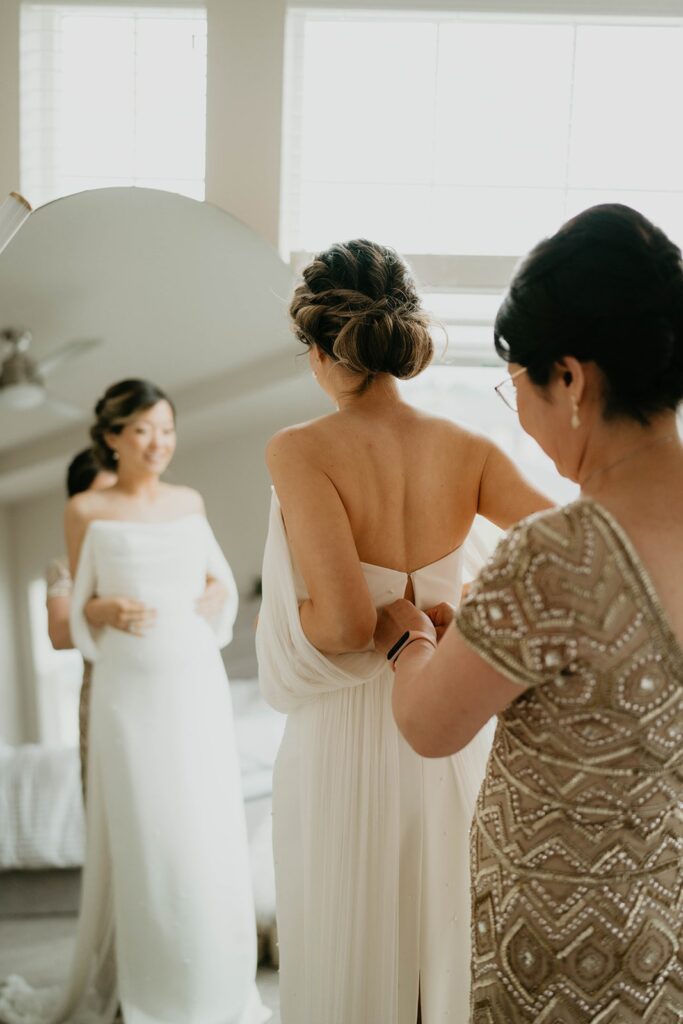 Mother helps bride into her white wedding dress at Asian wedding 
