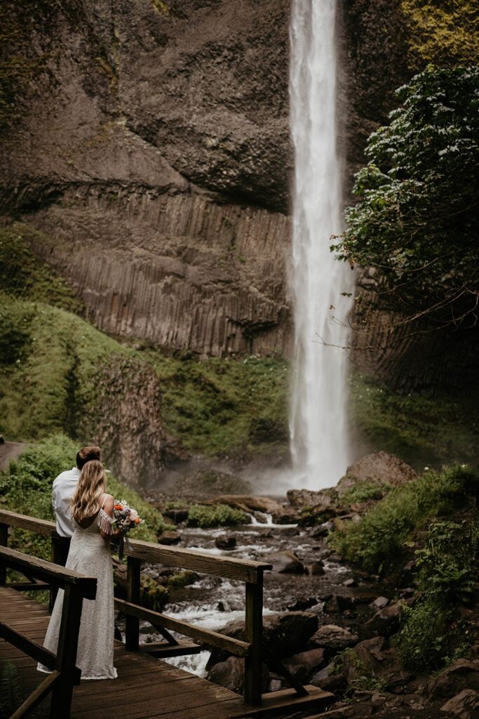 Bride and groom standing on a wood bridge looking at Latourell Falls