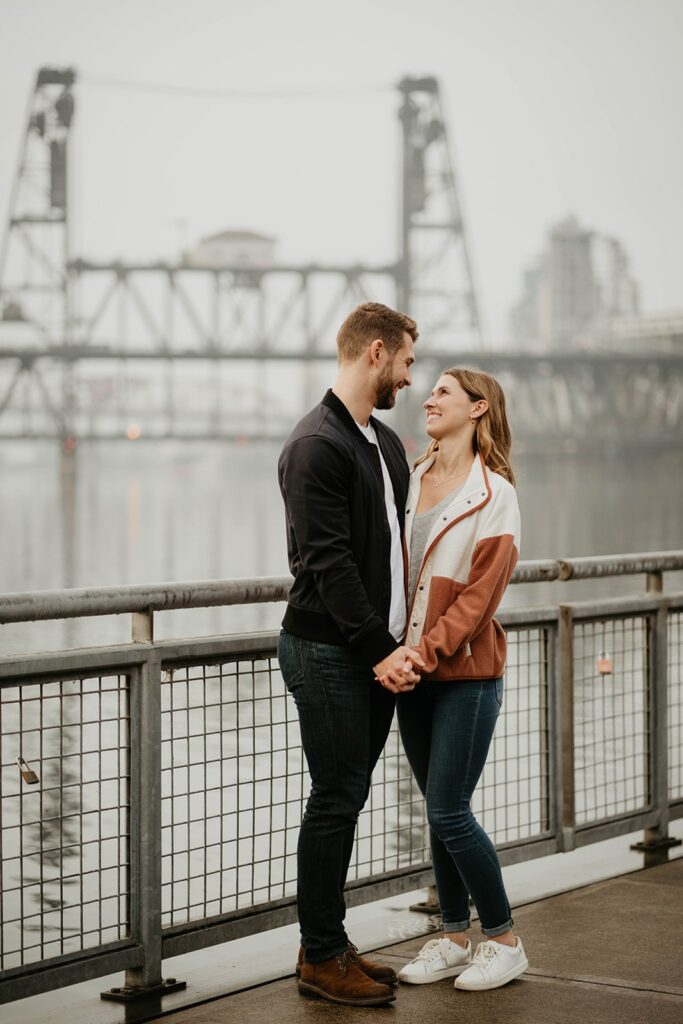 Couple holding hands and smiling during Portland engagement photo session by the river