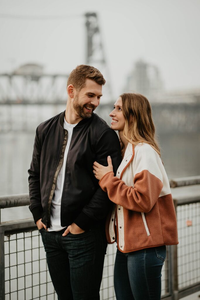Couple holding hands and smiling during Portland engagement photo session by the river