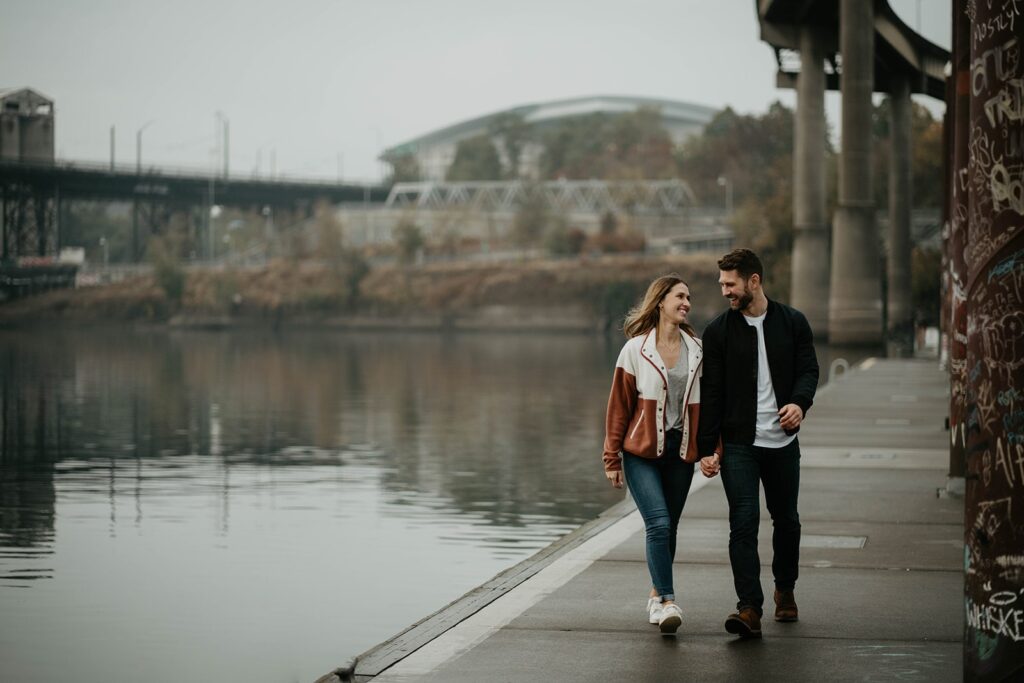 Couple walking hand along the river during Portland engagement photo session