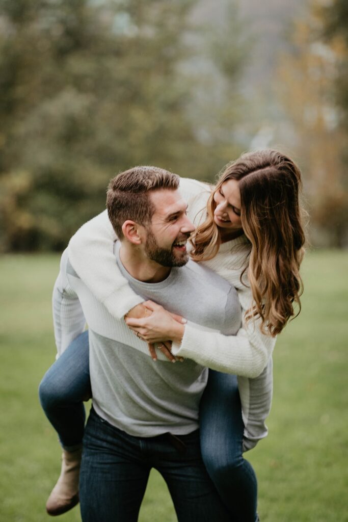 Woman riding on man's back during Cathedral Park, Oregon engagement photos