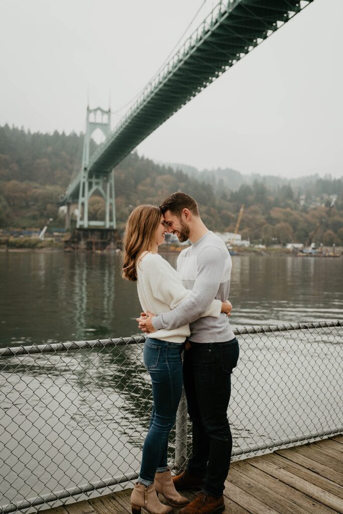 Couple hugging on a dock during their fall engagement photos at Cathedral Park, Oregon