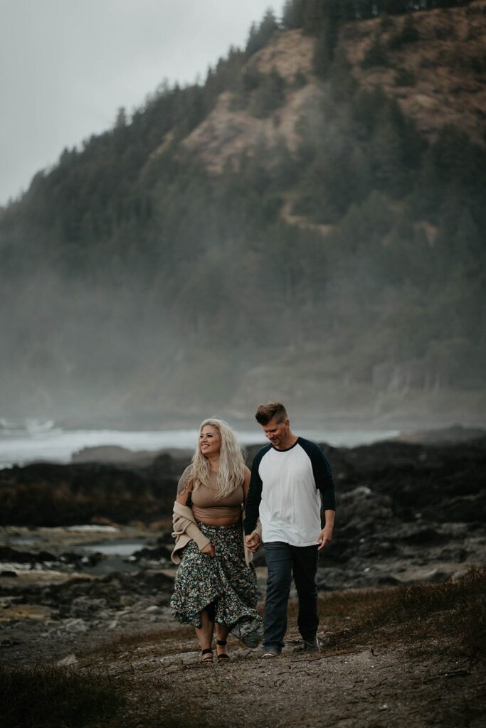 Couple walking on the rocky beach during their engagement session at Cape Perpetua