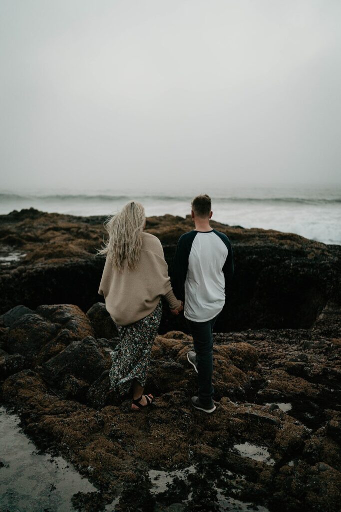 Couple holding hands while walking down to the beach for their Oregon Coast engagement photos