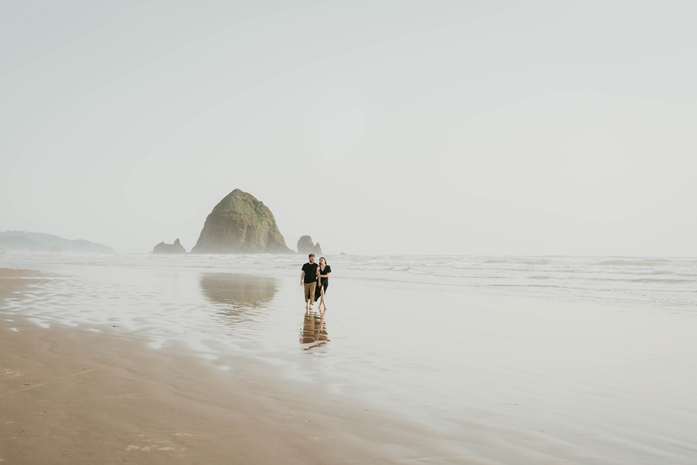 a couple walking along Cannon Beach with Haystack Rock in the background. 
